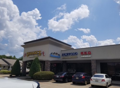Exterior of a restaurant building with signs for "Shane's Seafood" and "BBQ" under a blue sky with fluffy clouds.