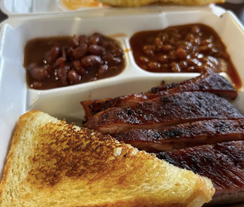 A takeout container with grilled meat, baked beans, red beans, and a slice of toasted bread.