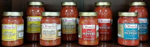 A display of jars labeled "Oliverio" containing sweet and hot peppers on a wooden shelf.