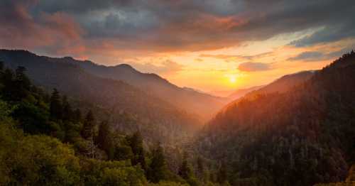 A breathtaking sunset over a misty mountain valley, with vibrant orange and yellow hues illuminating the sky.