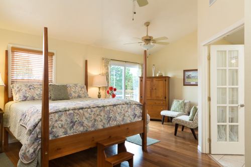 Cozy bedroom with a four-poster bed, wooden furniture, and large windows letting in natural light.