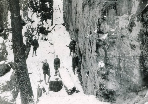 Black and white photo of people navigating a snowy, rocky canyon, with some climbing and others walking along the path.