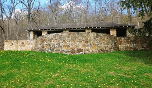 A stone building with a curved wall, surrounded by green grass and trees under a clear blue sky.