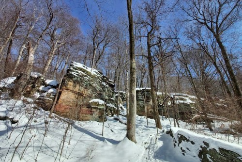 Snow-covered rocky landscape with bare trees under a clear blue sky.
