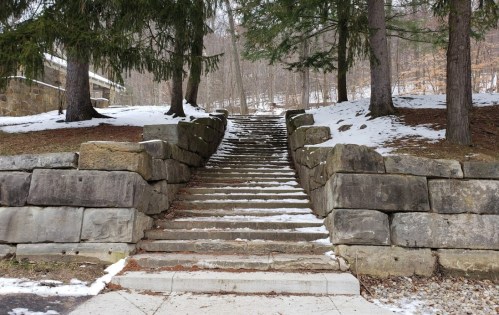 Stone steps lead up through a snowy landscape, flanked by trees and rocky walls.