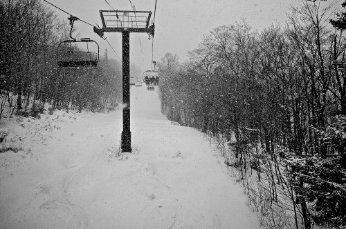 A snowy landscape with a ski lift and trees, creating a serene winter scene. Snowflakes are falling heavily.
