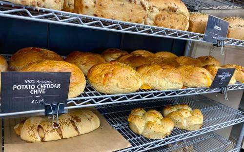 Freshly baked breads on a display rack, including potato cheddar chive loaves and braided bread.