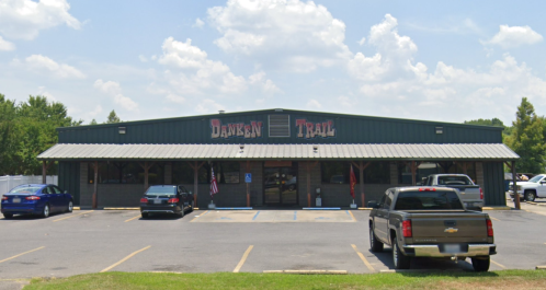 A green building with a sign reading "Dawson Trail," featuring parked cars and a clear blue sky.