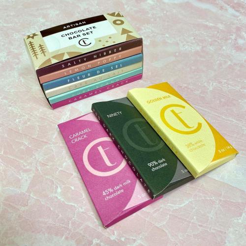 A collection of colorful chocolate bars stacked on a pink surface, featuring various flavors and designs.