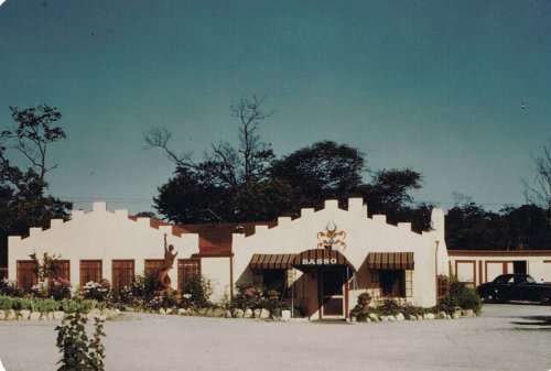 A charming building with a decorative facade, surrounded by trees and flowers, featuring a sign that reads "Basso."