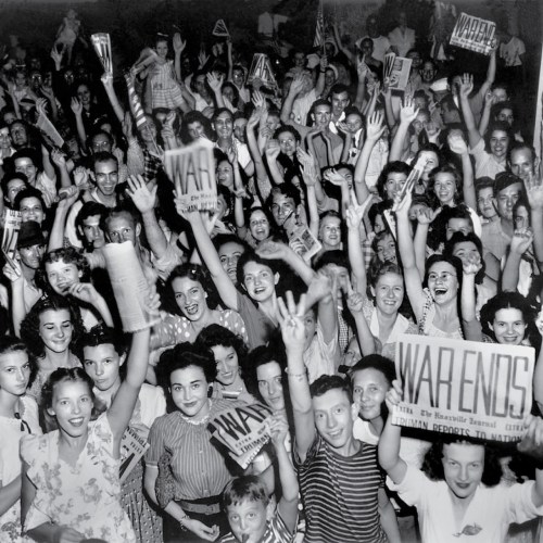 A large crowd of people celebrating, holding signs and cheering, with joyful expressions and raised hands.