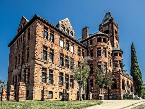 Historic red brick building with intricate architecture, featuring towers and large windows against a clear blue sky.