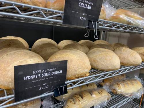 Freshly baked loaves of sourdough and challah bread displayed on a shelf with price tags.