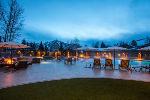 A serene pool area at dusk, surrounded by lounge chairs and umbrellas, with mountains in the background.