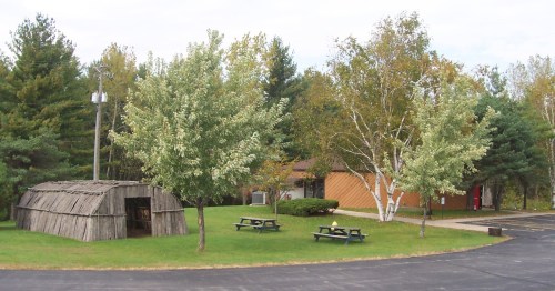 A grassy area with trees, a wooden structure, and a building in the background, surrounded by a paved path.