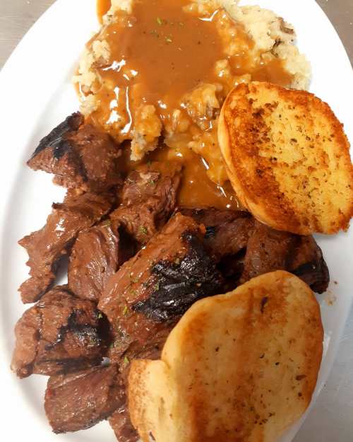 A plate of grilled steak, mashed potatoes with gravy, and toasted bread.