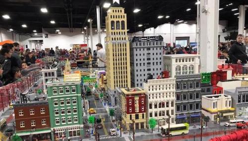 A detailed LEGO cityscape with tall buildings, streets, and crowds of people at a convention.