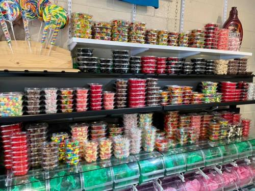 A colorful display of various candies in clear containers on shelves, with lollipops in the background.