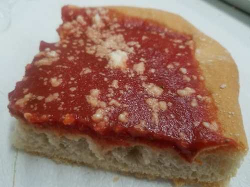 A slice of pizza with a thick layer of red sauce and a sprinkle of cheese on a soft crust.