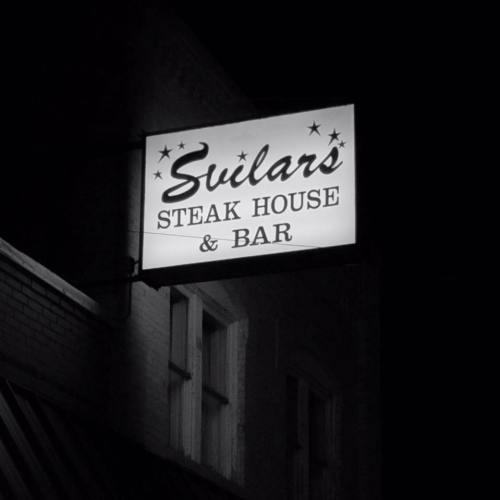 A vintage sign for "Swilar's Steak House & Bar" illuminated against a dark background.