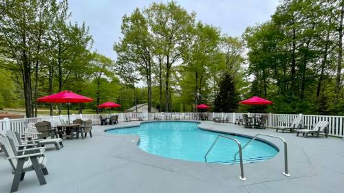 A serene pool area surrounded by trees, featuring red umbrellas and lounge chairs on a gray deck.