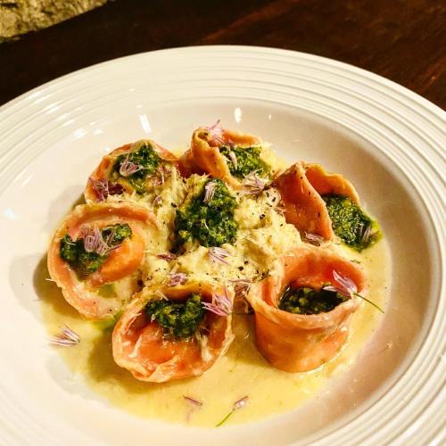 A plate of pasta filled with green pesto, garnished with herbs and edible flowers, served in a creamy sauce.