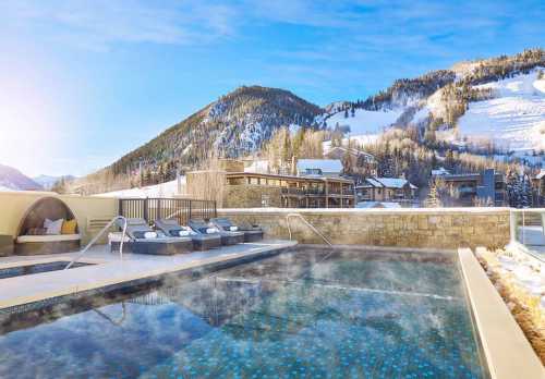 A serene outdoor hot tub with mountain views, surrounded by snow-covered trees and a clear blue sky.