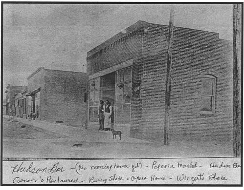 Historic black-and-white photo of a brick building with two people and a dog outside, labeled "Hudson Ber."
