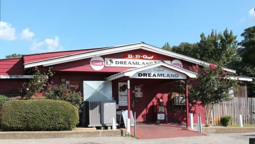 Exterior of Dreamland BBQ restaurant, featuring a red building with signage and a clear blue sky.