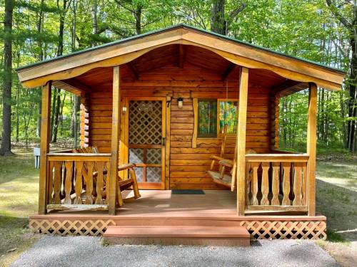 A cozy wooden cabin with a porch, surrounded by lush green trees in a serene outdoor setting.