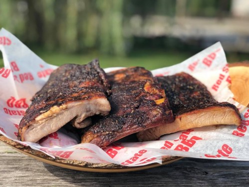 A basket of grilled ribs with a smoky, charred exterior, served on red and white paper.