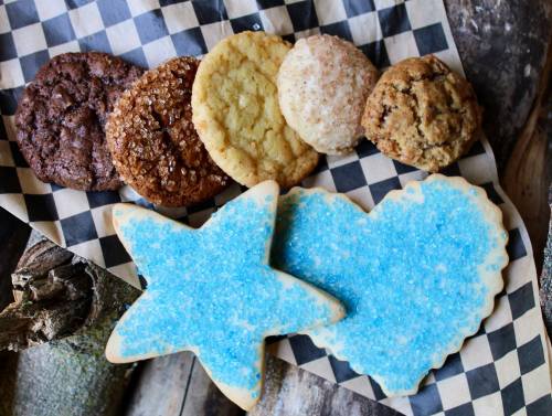 A variety of cookies, including chocolate, sugar, and decorated star and heart-shaped cookies, on a checkered paper.