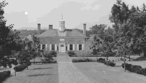 Historic building with a central cupola, surrounded by trees and a landscaped pathway. Black and white photo.