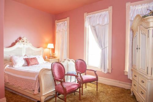 Cozy bedroom with a pink color scheme, featuring a bed, two chairs, and large windows with white curtains.