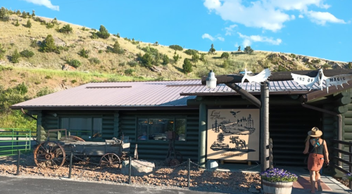 A rustic log cabin with a sign reading "End of the Magic," surrounded by hills and a person walking towards it.