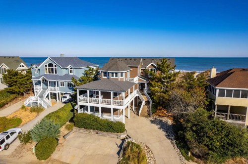Aerial view of beach houses near the ocean, with clear blue skies and greenery surrounding the properties.