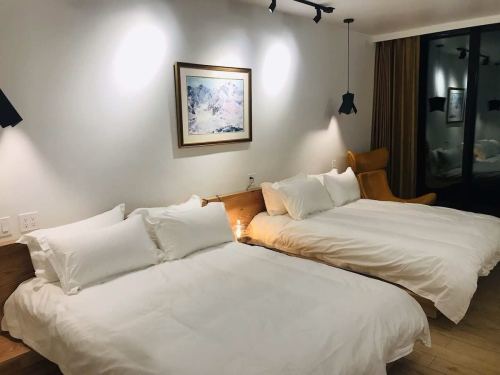 A cozy hotel room featuring two beds with white linens and a stylish armchair, illuminated by soft wall lights.
