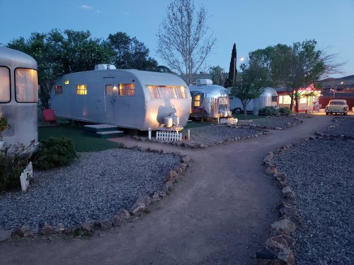 A vintage trailer park at dusk, featuring several retro trailers surrounded by gravel paths and greenery.