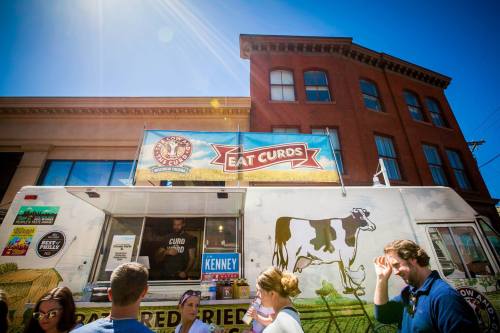 A food truck named "Eat Curds" with a cow graphic, surrounded by people enjoying the sunny day.