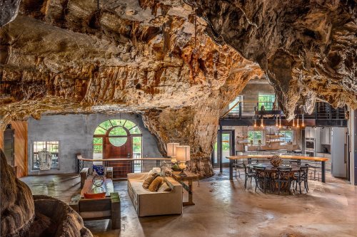 A unique cave-inspired living space with natural rock formations, modern furniture, and large windows.