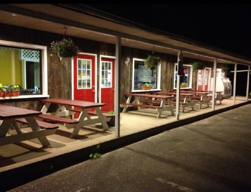A rustic building at night with red doors, picnic tables, and hanging plants along a covered porch.