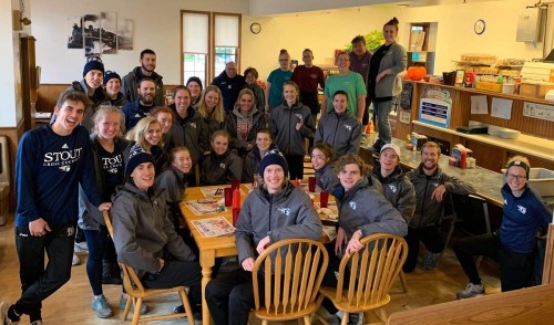 A group of cross country team members gathered in a cozy diner, smiling and wearing matching jackets and hats.