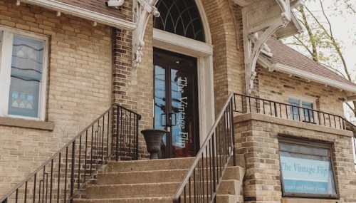 Entrance of "The Vintage Flip" with stairs and decorative windows, featuring a sign on the door and a window display.