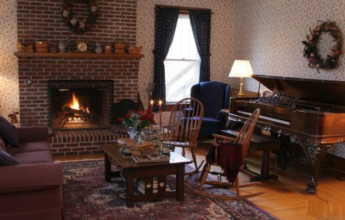 Cozy living room with a fireplace, piano, and comfortable seating, decorated with floral patterns and warm lighting.