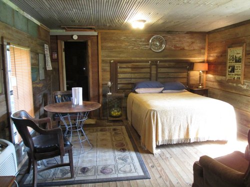 Cozy rustic bedroom with a wooden bed, table, and warm lighting, featuring a vintage decor and wooden walls.