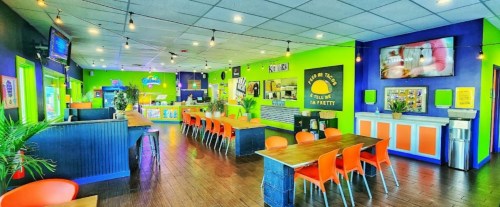 Brightly colored restaurant interior with orange chairs, wooden tables, and vibrant green and purple walls.