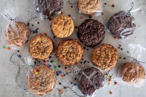 A variety of cookies, some wrapped in clear bags with black and white twine, scattered on a light surface.