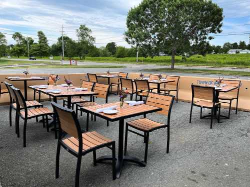 Outdoor dining area with empty tables and chairs, surrounded by greenery and a clear sky.