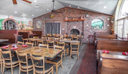 Interior of a restaurant featuring wooden tables and chairs, a brick wall, and decorative artwork.