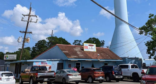 A blue building with a sign, surrounded by cars, next to a tall water tower under a partly cloudy sky.